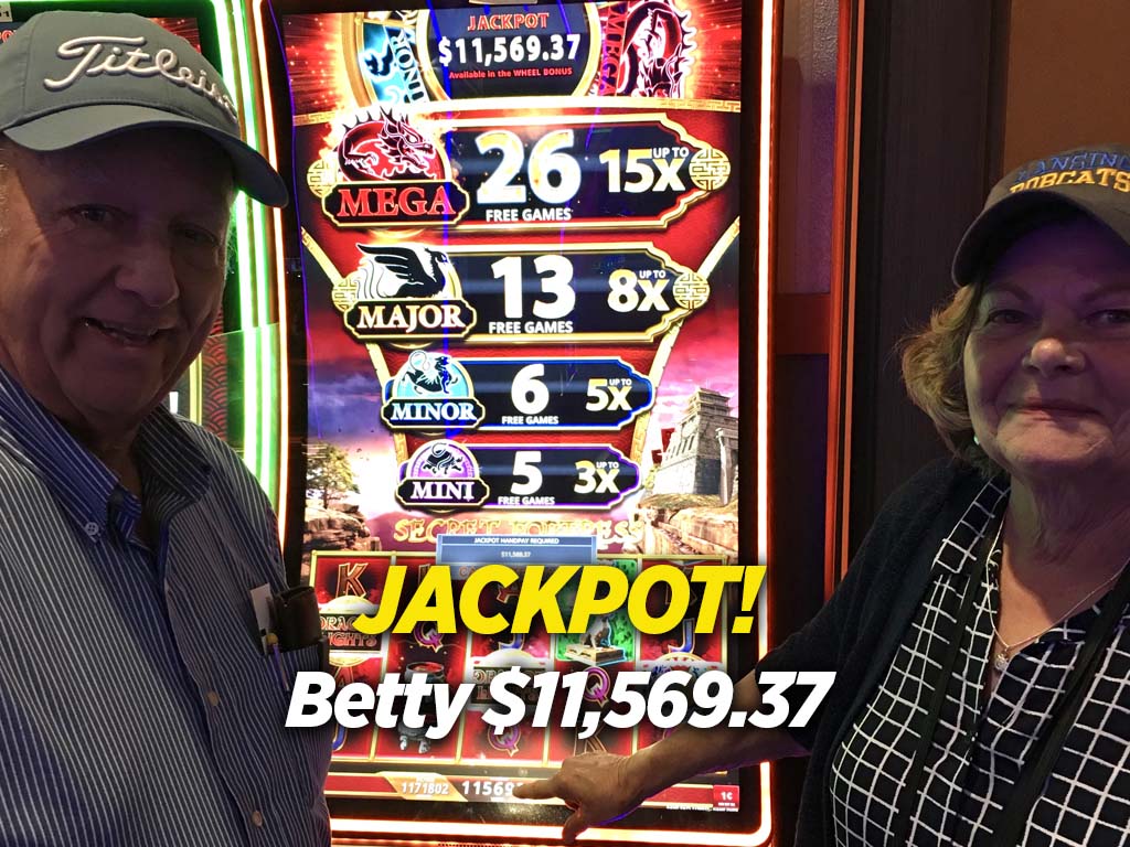 Two people standing in front of a slot machine that says jackpot.