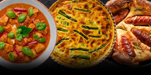 A bowl of curry with basil, an asparagus quiche, and a sausage toad-in-the-hole arranged in a row.