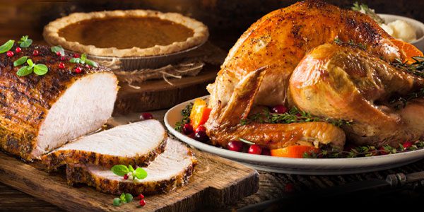 A cooked turkey and sliced roast are displayed with herbs, next to a pumpkin pie.