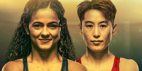 Two women wearing athletic tops stand side by side, looking straight ahead, with a blurred background and warm lighting.
