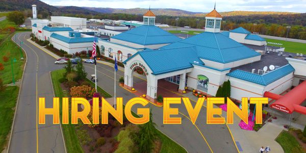 Aerial view of a large building complex with blue roofs, surrounded by roads and greenery. Large yellow text reads "HIRING EVENT.