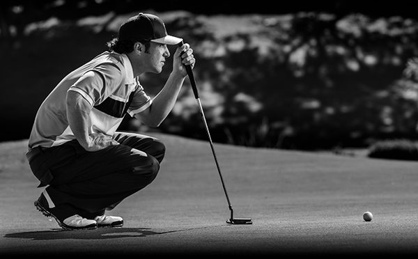 A man crouching down holding a golf club.