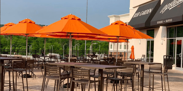 Outdoor patio dining area with several tables and chairs under bright orange umbrellas at a restaurant.